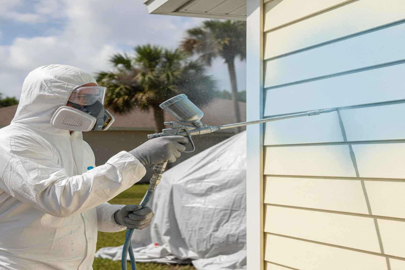Professional painter applying acrylic latex paint to vinyl siding with a sprayer